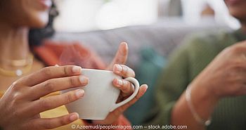 Zwei Frauen sitzen gemeinsam auf der Couch, trinken Kaffee und unterhalten sich.