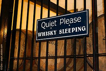 Schild mit der Aufschrift "Quiet Please Whisky Sleeping" vor einigen Holzfässern