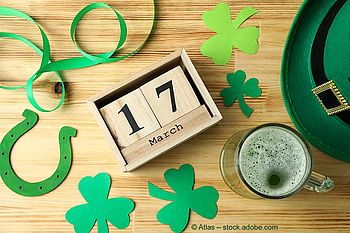 Verschiedene Accessoires zum St. Patrick's Day: grüner Hut, grünes Getränk, Papier-Kleeblätter und Luftschlangen, Datumsangabe 17. März