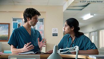 "This Is Going To Hurt - Sisyphos ist müde": Shruti (Ambika Mod) und Adam (Ben Whishaw) lehnen an der Rezeption einer Krankenstation und unterhalten sich.