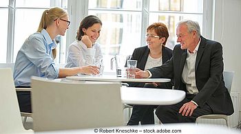 Drei Frauen und ein Mann sitzen an einem Tisch im Büro und unterhalten sich.