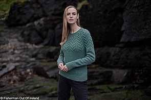 Ein weibliches Model trägt einen grünen Zopfstrickpullover von Fisherman out of Ireland.