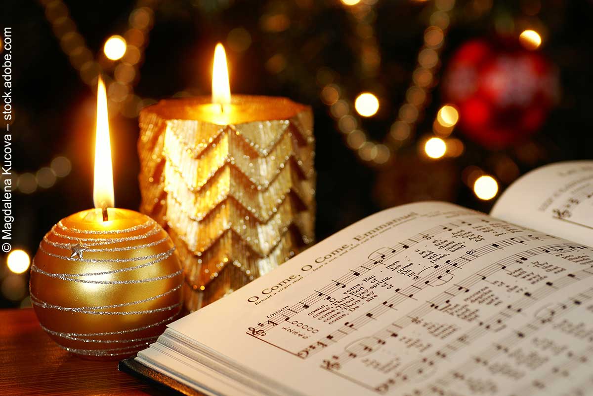 Zwei Kerzen und ein Liederbuch mit Christmas carols auf einem Tisch