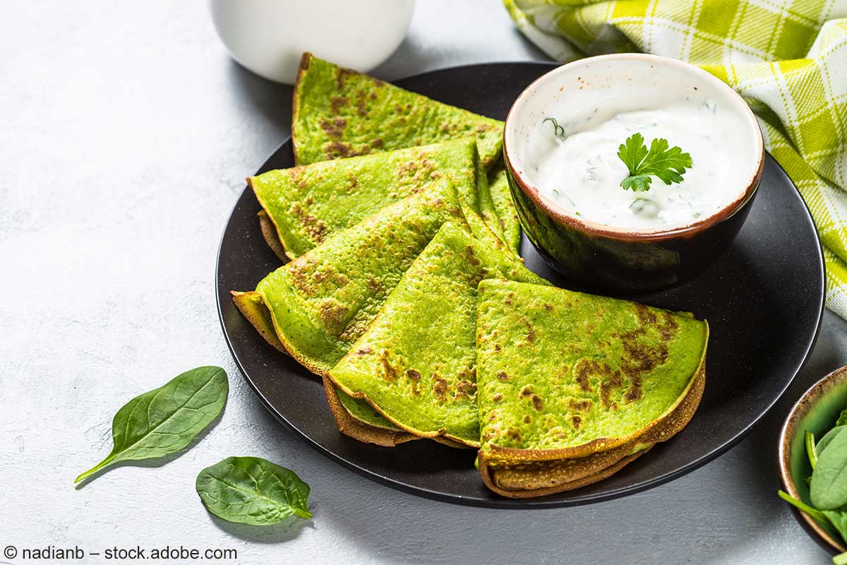 Durch Spinat grüngefärbte Pancakes mit Joghurt-Kräuter-Dip auf einem Teller