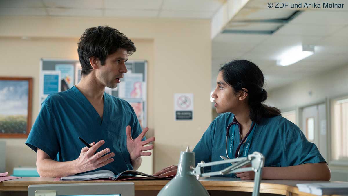 "This Is Going To Hurt - Sisyphos ist müde": Shruti (Ambika Mod) und Adam (Ben Whishaw) lehnen an der Rezeption einer Krankenstation und unterhalten sich.